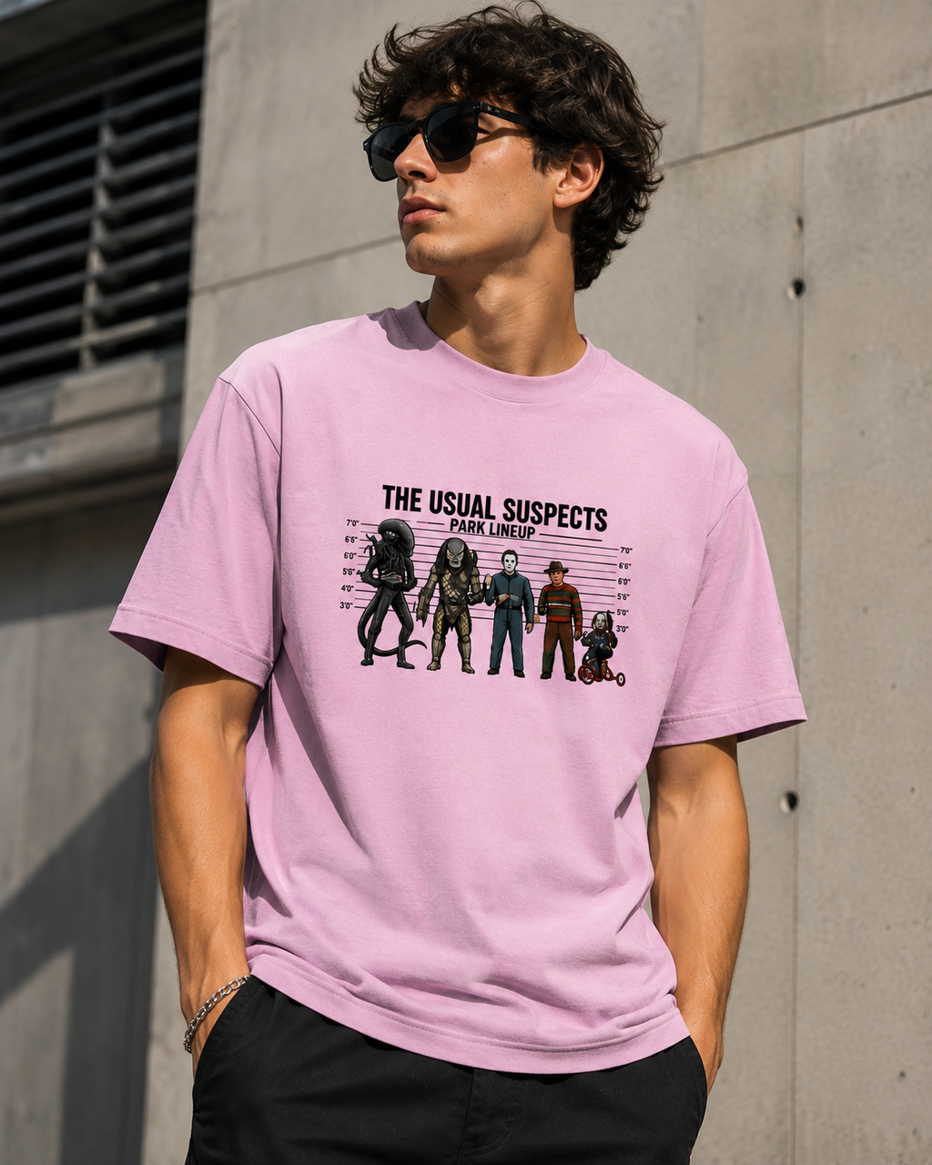 A man wearing a light pink graphic t-shirt with a 'The Usual Suspects' character print, standing against a concrete wall.