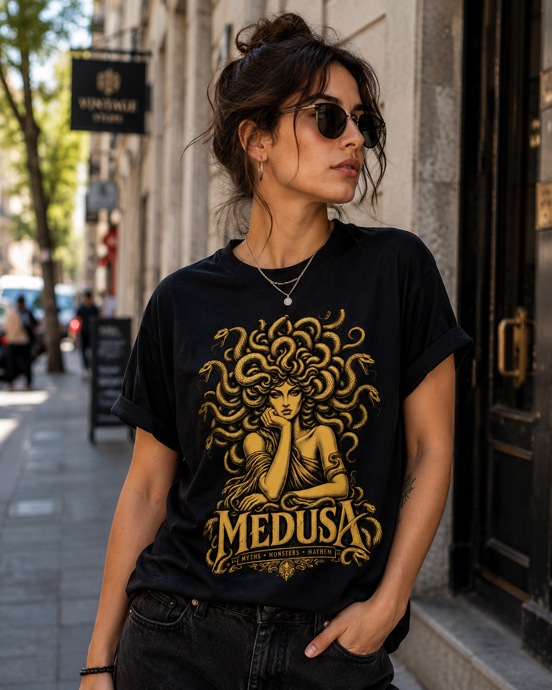 A woman wearing a black graphic t-shirt with a gold Medusa print, standing on a city street.